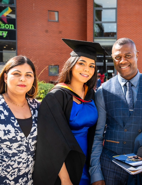 Student wearing graduation gown posing with parents