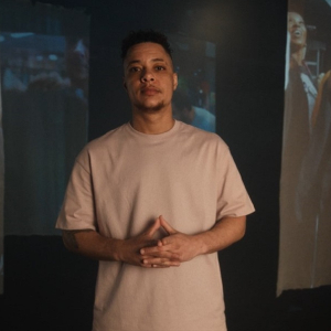 Nate Ethan Watson wearing a white shirt against a backdrop of projected images