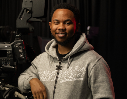 Photograph of Theo Johnson with a film camera on a darkened set