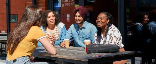 Students drinking coffee together at an outdoor table in the courtyard of Wolverhampton City Campus