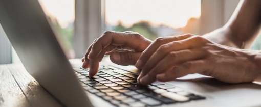 A laptop on a table being operated by the hands of a person out of frame.