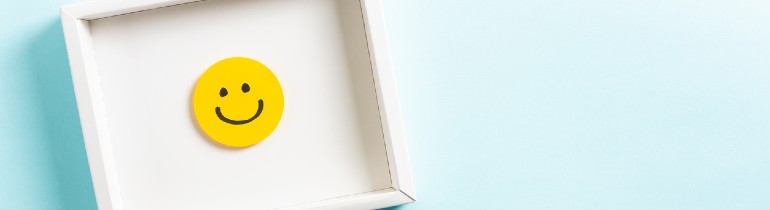 Image of a smiley face within a square white frame hung on a light blue wall.