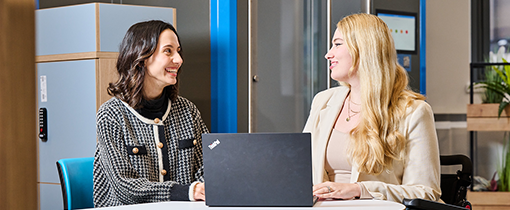 two smiling women having a one to one discussion with a laptop in front of them on the table