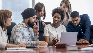 A group of students from global majority backgrounds seated around a laptop on a table.