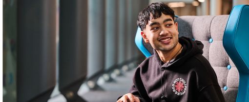 Male student looking past camera and smiling whilst sitting down with tablet