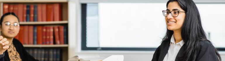 A female student smiles in a courtroom wearing legal attire