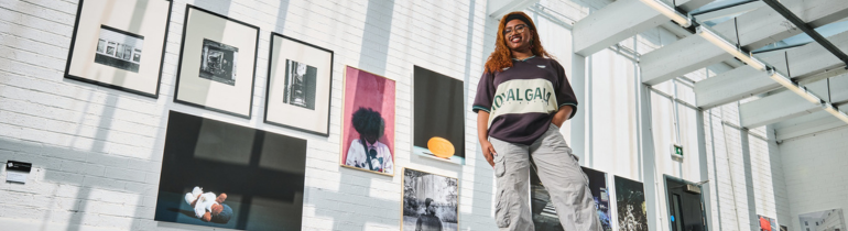 A female student smiles in front of art work in a gallery space