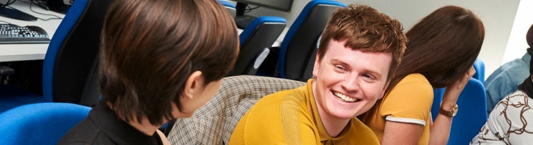 a male student in a yellow jumper smiles at a female student