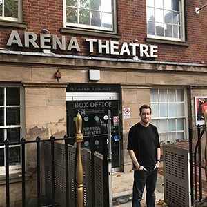Neil Reading Artistic Director of the Arena Theatre, photographed outside the theatre's main entrance in Wulfruna Street in Wolverhampton. You can see the Arena Theatre sign that hangs above the entrance in the background of this image. Neil is wearing a black crew neck jumper, he is smiling.