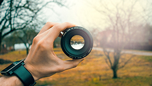 A camera lens held in the hand of the photographer and pointed towards a lake