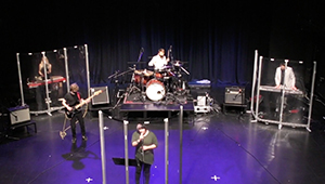 A band of improv musicians: Singer, guitarist, drummer and keyboardist, performing under purple stage-lights
