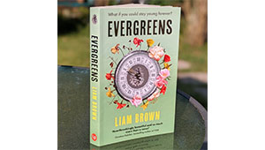 A paperback copy of EVERGREEN by Liam Brown stood on a table with its cover facing the camera