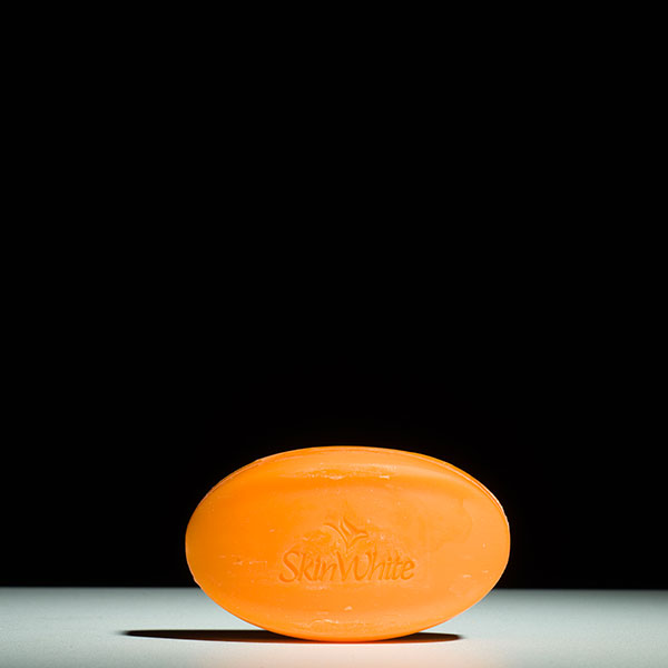 Photograph of an orange bar of soap on a white surface against a black background.
