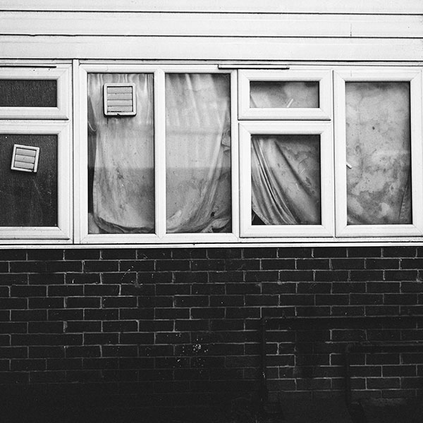 Black and white photograph of windows covered up by curtains on the opposite side from the camera.