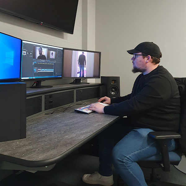 James Gurdin at a computer desk editing a video across three monitors, one used to view the video, another the editing timeline, the third currently not being used