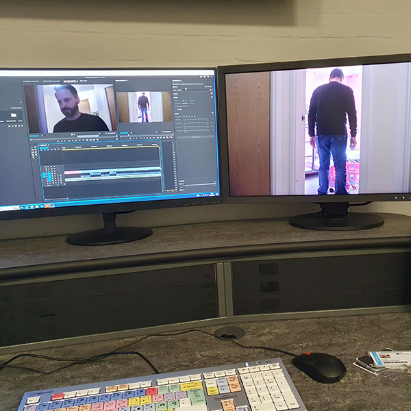 A two-monitor setup showing a video edit in-progress, the left display showing a video timeline and the right showing a still from the video itself: a man standing in a doorway with his back to the camera