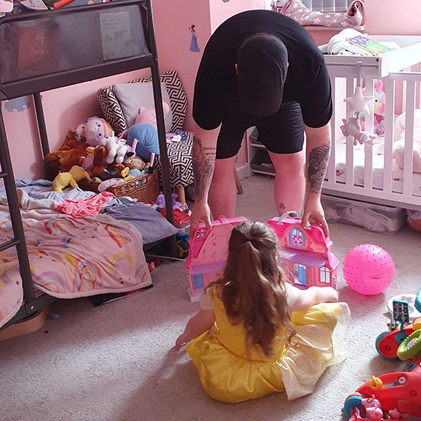 A man interacting with a young child in her bedroom, helping her to play with a dollhouse