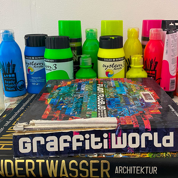 An array of paint bottles and cans on a table-top with two books about graffiti.