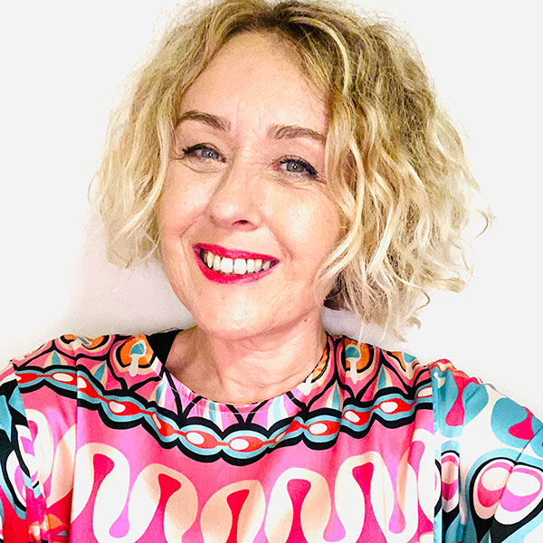 A photograph of Keri Hunt in a white studio wearing a patterned blouse.