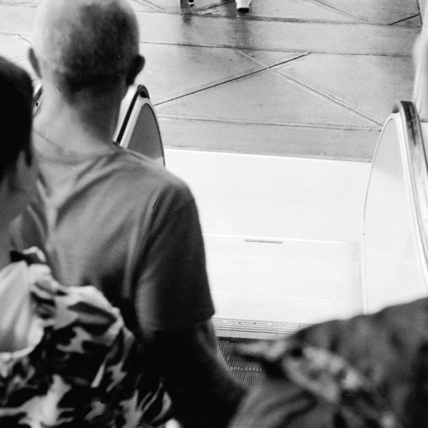 Black and white photograph of people descending to the bottom of an escalator.