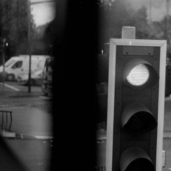 Black and white photograph of a traffic light captured from the window of a vehicle.