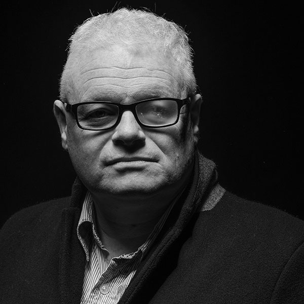 Black and white portrait photograph of a man wearing glasses with one lens visibly cracked.