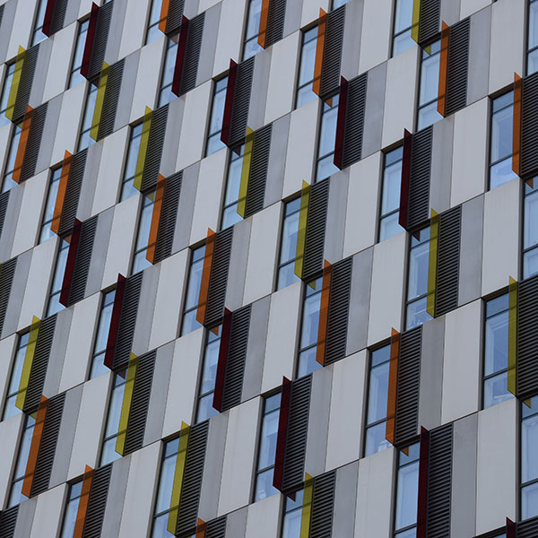 Picture of lines of windows along the side of a large block of flats, situated asymmetrically in ascending rows with variably coloured windowpanes.
