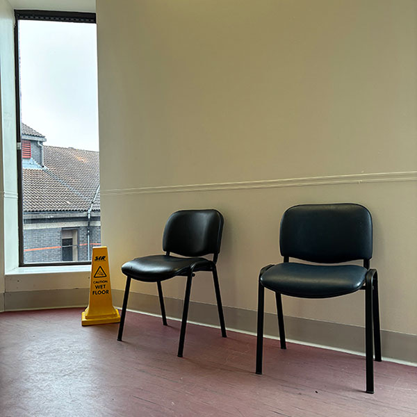 Two small black leather chairs against a wall next to a yellow conical wet floor sign, a large window on the far wall next to this arrangement.