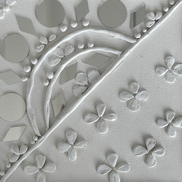 A piece of square artwork constructed of clay and reflective silver material on a white canvas, consisting of various circle, diamond and petal shapes arranged in sequence.