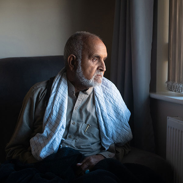 Picture of a seated man looking out of a window, a purple candle standing on the windowsill.