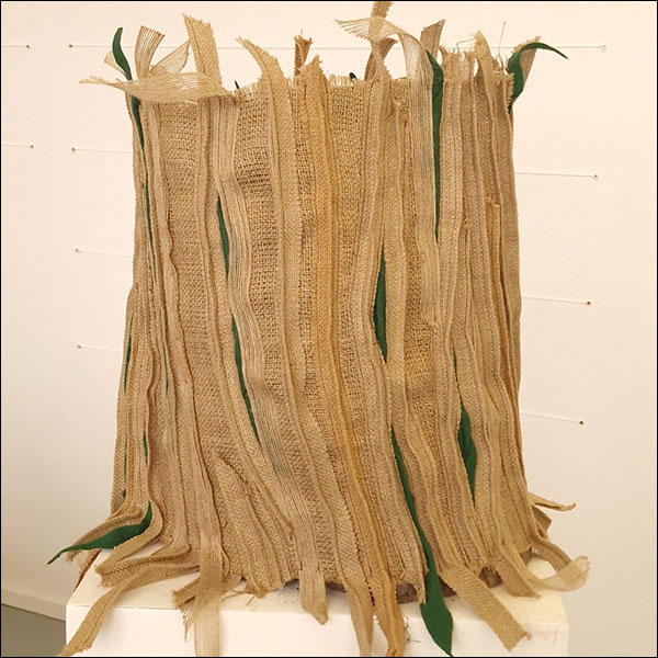 An arrangement of beige and green fabrics bundled cylindrically together, resembling a tree trunk.