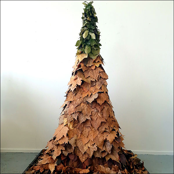 An arrangement of brown leaves arranged in the shape of a tree, green leaves used at the top of the structure reaching to a single point.