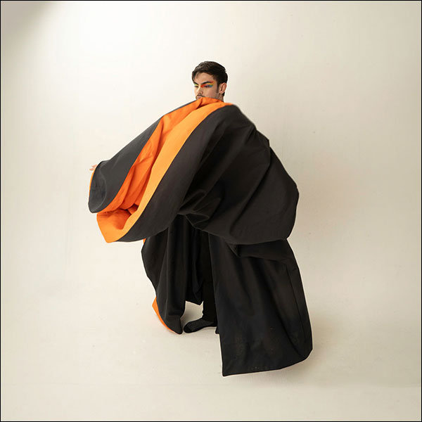 A student with multicoloured eyeshadow photographed in large billowing graduate robes.