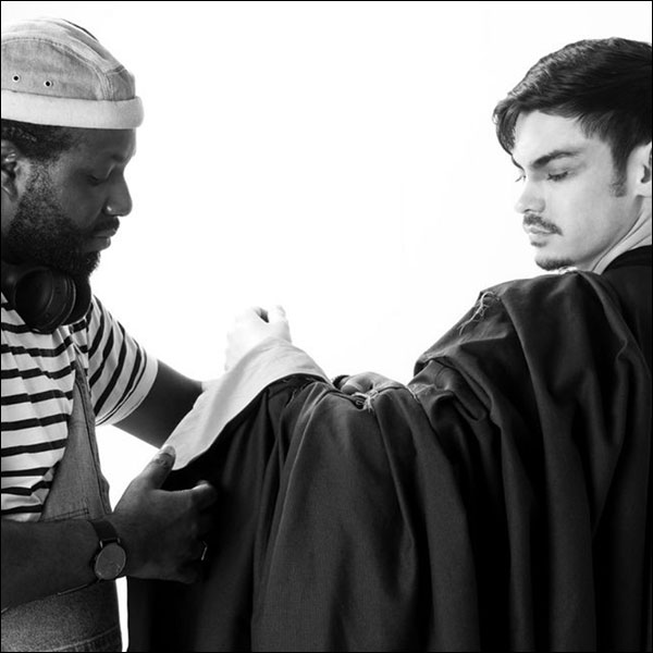 Black and white photograph of a student being dressed in graduation robes.