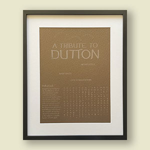 Framed poster showcasing the Dutton Cast typeface. poster contains various letter forms and text in black printed on a brown background. Poster is mounted on white card and framed by a black frame.