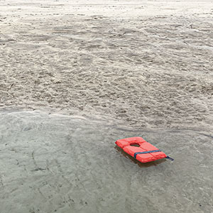 Photograph of a life jacket, washed ashore on an empty beach