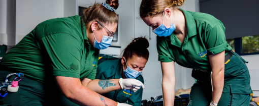 Three students wearing green nursing clothes, protective gloves and face masks.