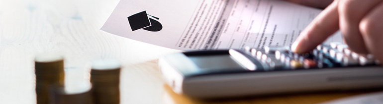Student sat at desk looking at student fee form while using a calculator. There is also a stack of coins on the table.