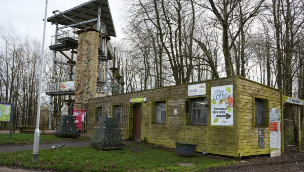 Exterior of a Sky Reach facility with signage pointing towards it entrance, a tall climbing wall visible in the background