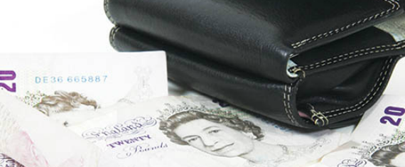 A black leather wallet on a white table-top with three £20 notes