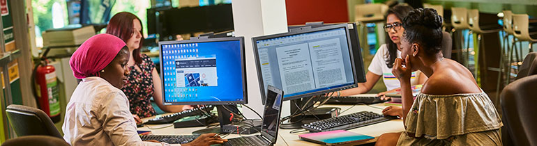 Postgraduate students seated around a square table, each working on their own desktop computers.