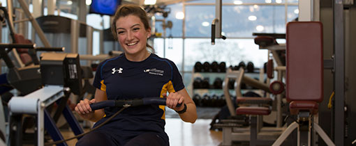 A woman in the gym at Walsall campus, wearing University of Wolverhampton branded sports clothing and using a rowing machine