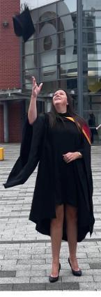 Suzanne in graduation gown throwing cap in the air, looking up towards the sky