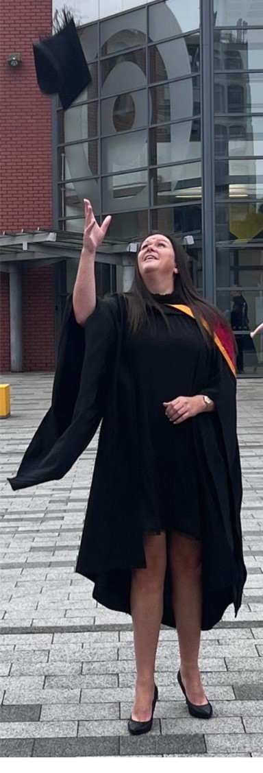 Suzanne in graduation gown throwing cap in the air, looking up towards the sky