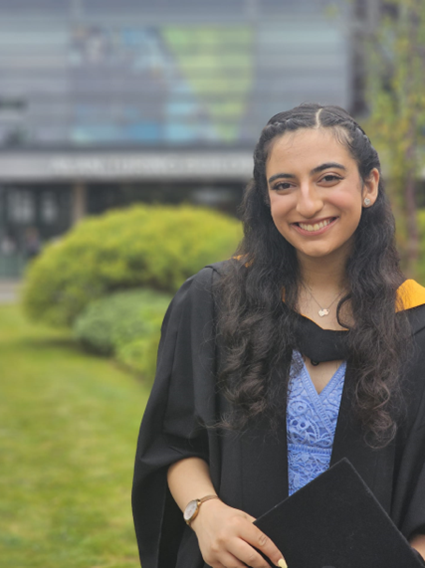 Student Karisma standing outside wearing graduation gown