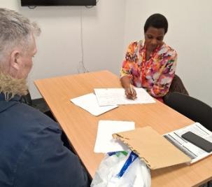 Student Emily sitting at table, writing on paper with male sitting opposite