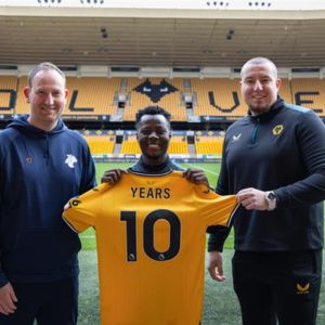 Three males holding up Wolverhampton Wanderers T-shirt on football pitch