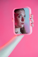 a photo of a girl in a mirror with a pink background