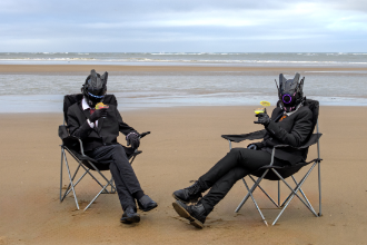 a photo of two men in suits and masks on a beach