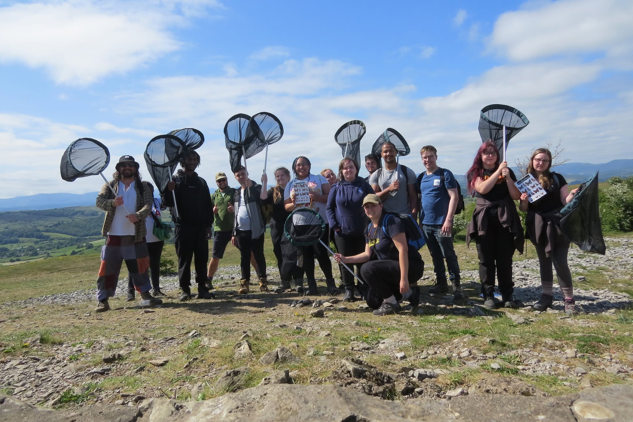 Students standing on top of a grassy hill holding bug nets on a field trip.